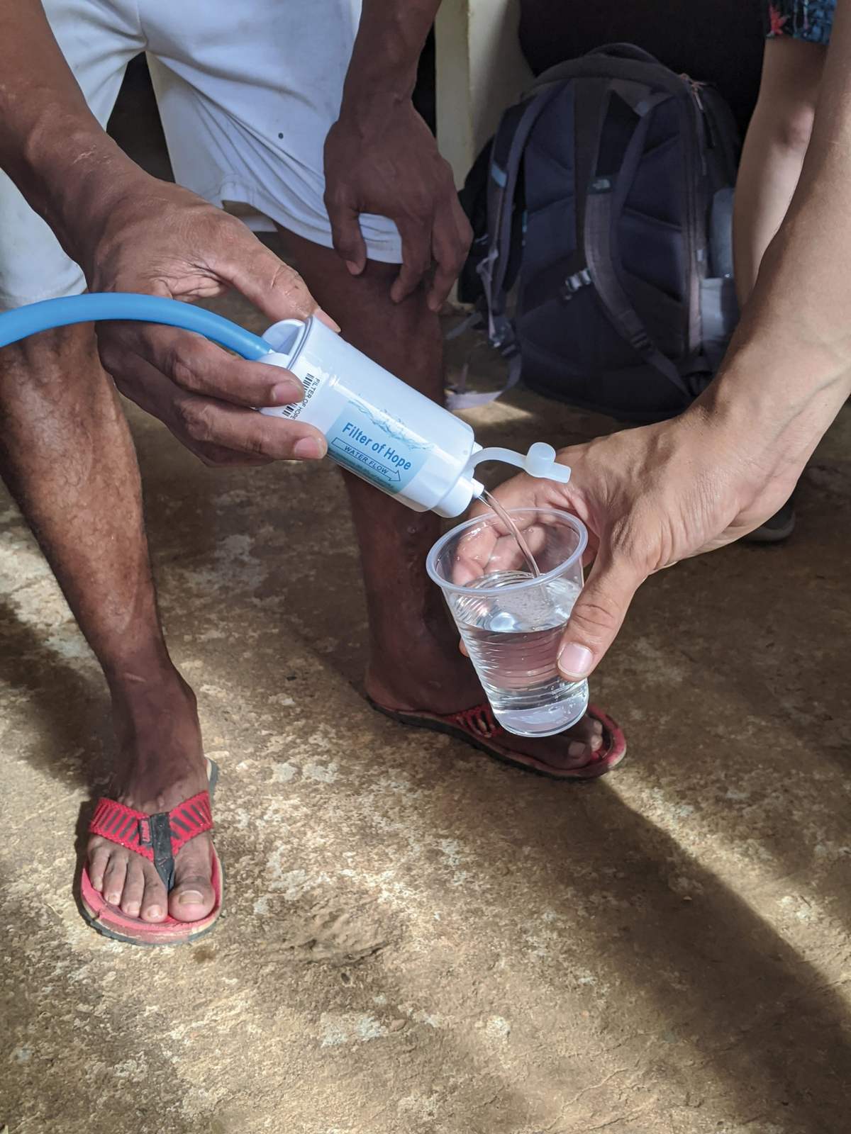 Clean water flows from a Filter of Hope filter into a cup