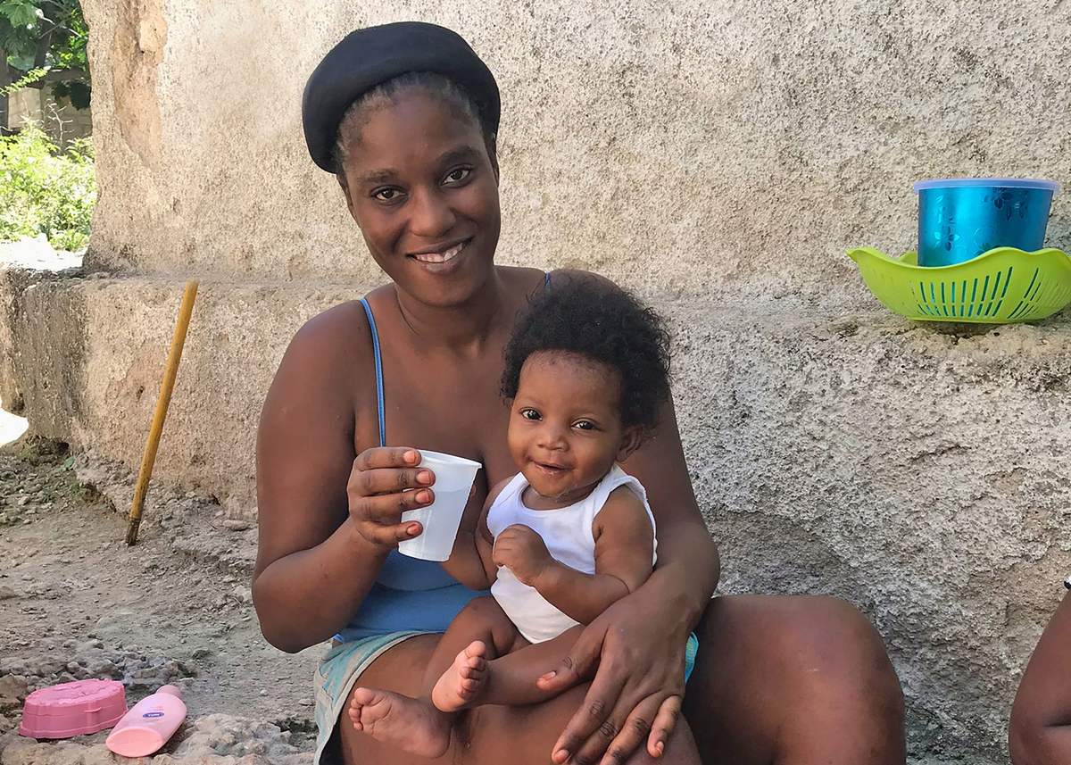 A mother and her baby smile as they hold cups of clean water
