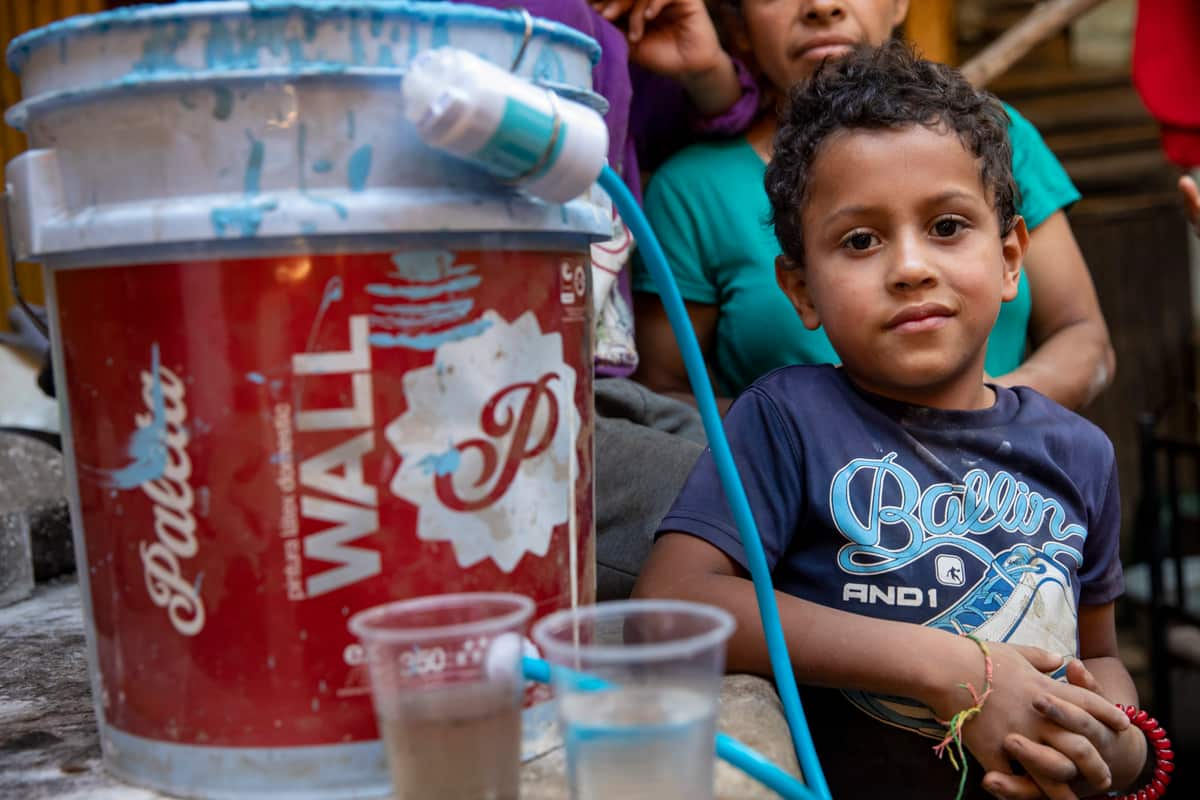 A boy holds a cup of clean water next to a cup of the dirty water his family used to drink