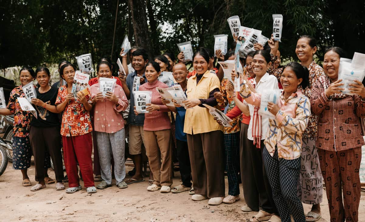 A large crowd of women raises cups of clean water and Gospel booklets