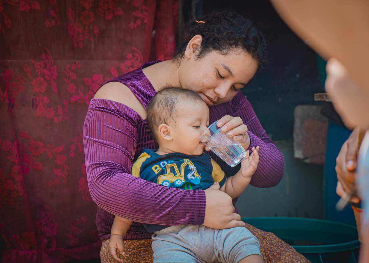 A mother helps her baby drink clean water from a cup
