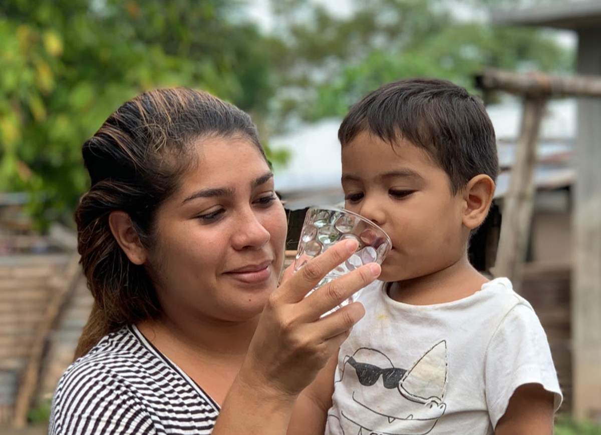 A mother holds a cup of clean water to her young son's lips