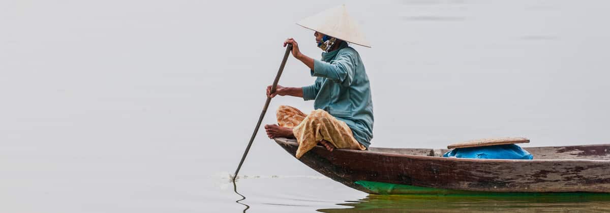 A man paddles a wooden boat on a river in Laos