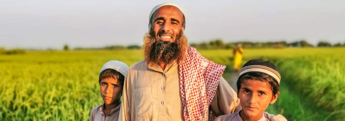 A father and his two sons stand in a green field in Pakistan