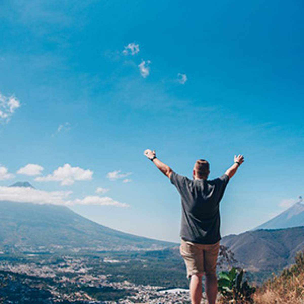 A trip member raises his arms on a mountain overlooking a valley town