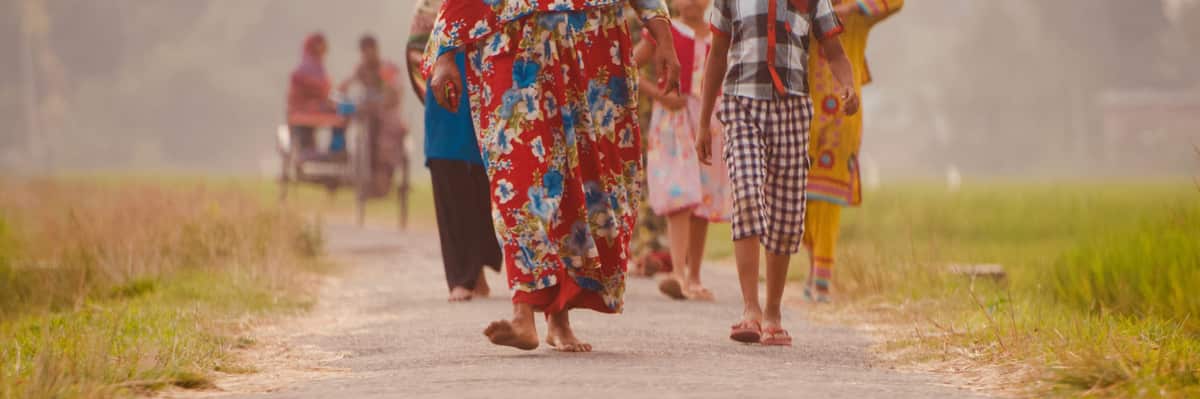 Women in bright saris walk along a dirt road in India