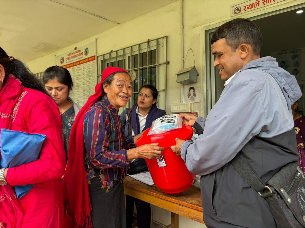 A church volunteer hands a red filter bucket to an older woman in Nepal