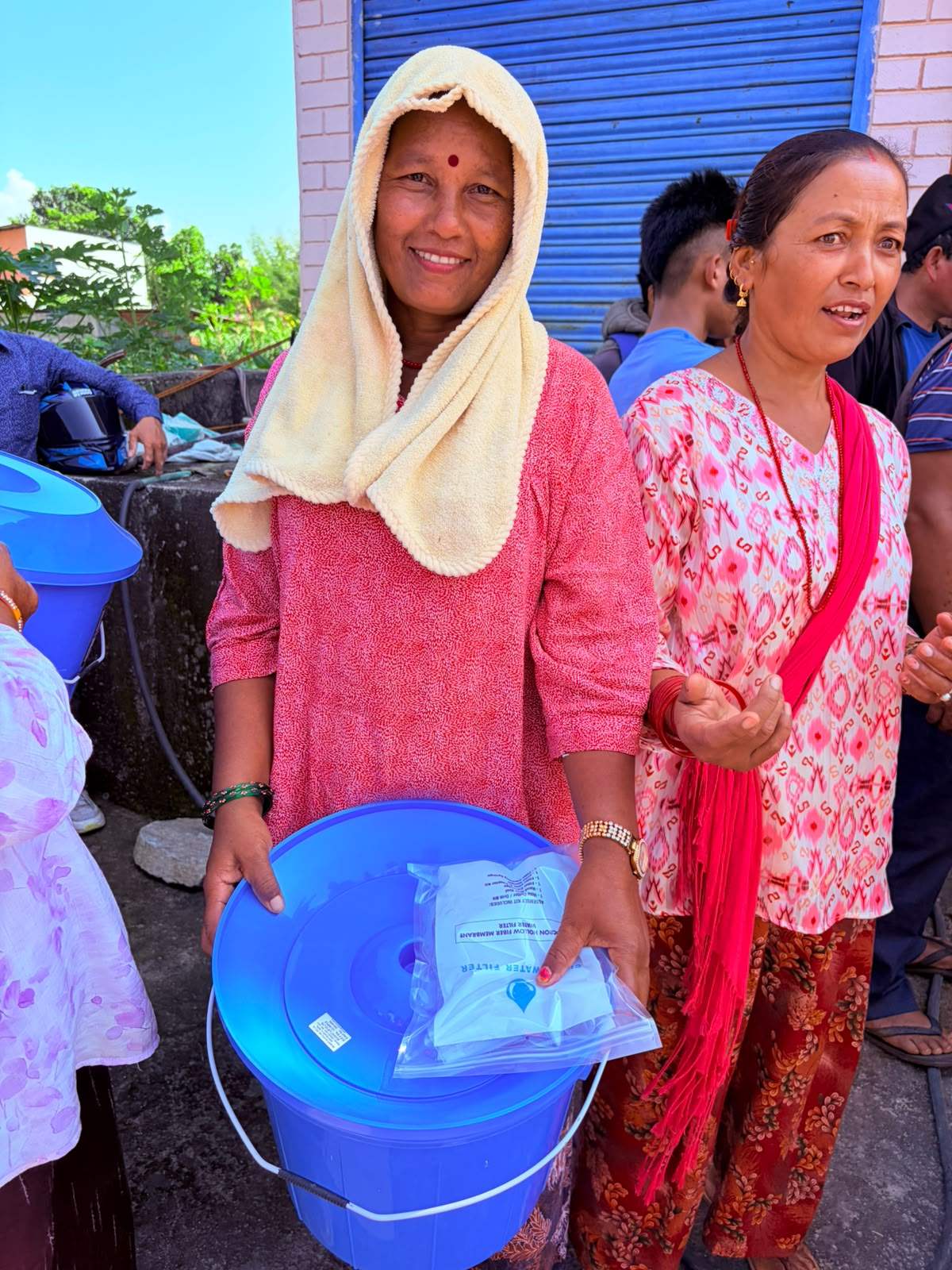 A woman in Nepal smiles as she holds her new blue filter bucket