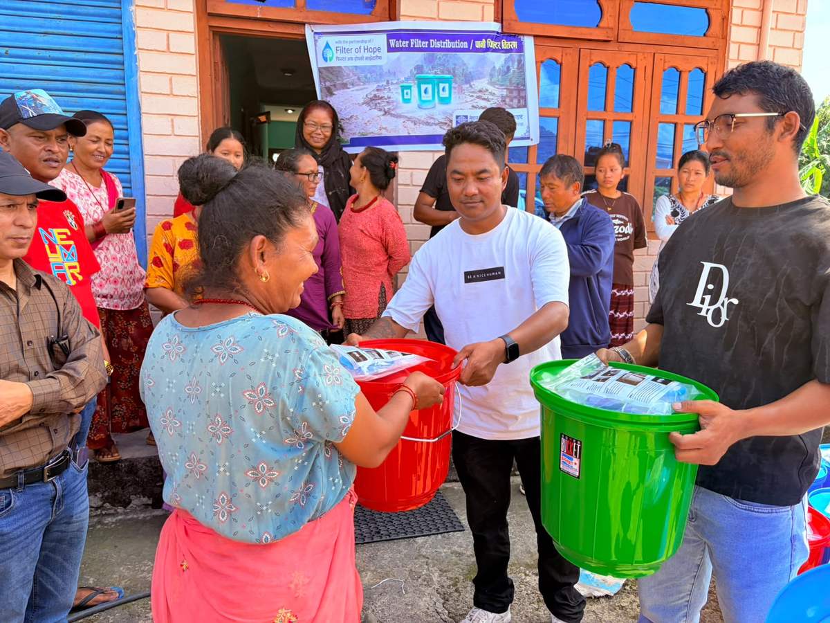 Volunteers hand green and red filter buckets to flood survivors in Nepal