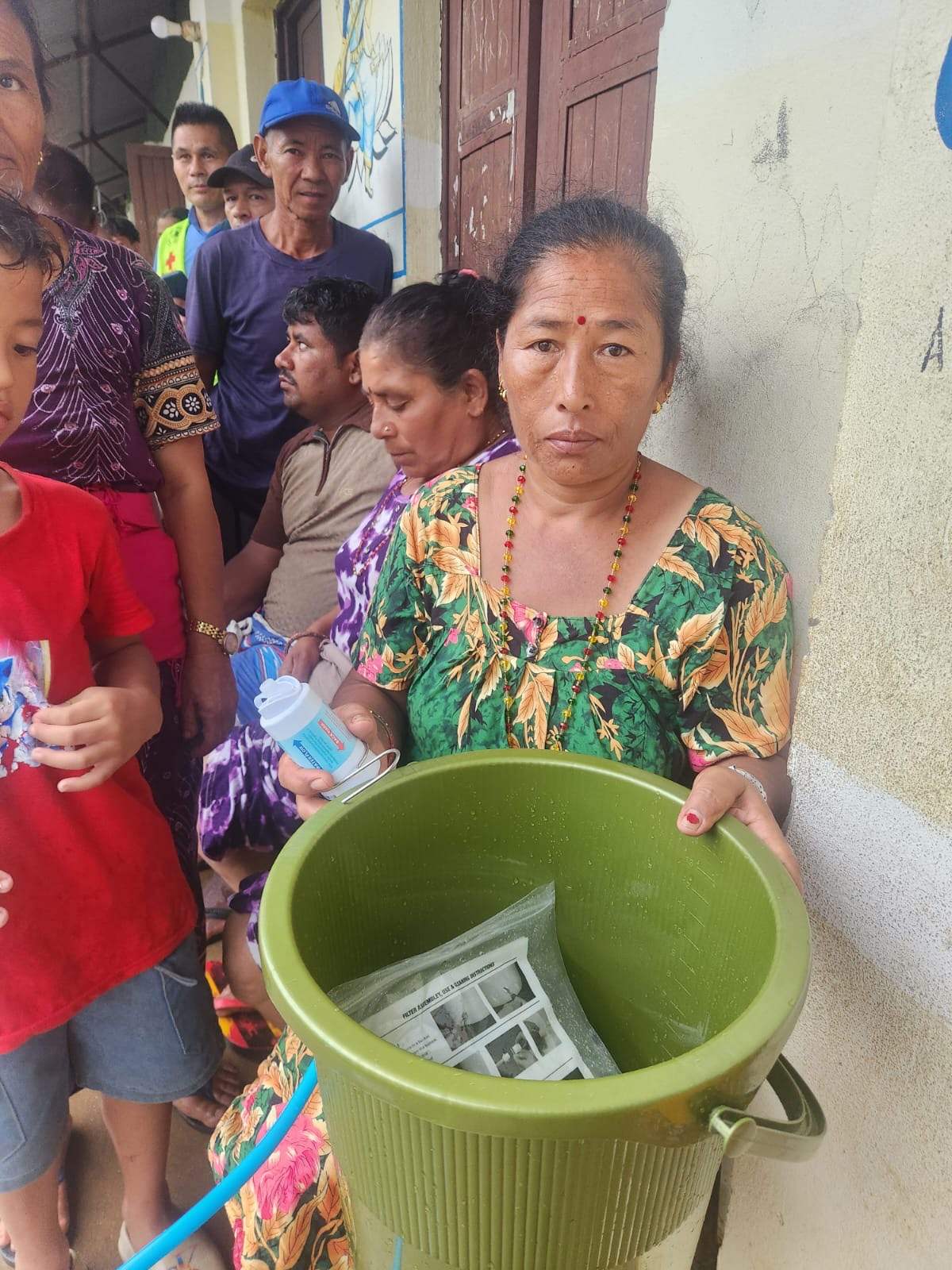 A woman in Nepal holds a green filter bucket among flood survivors