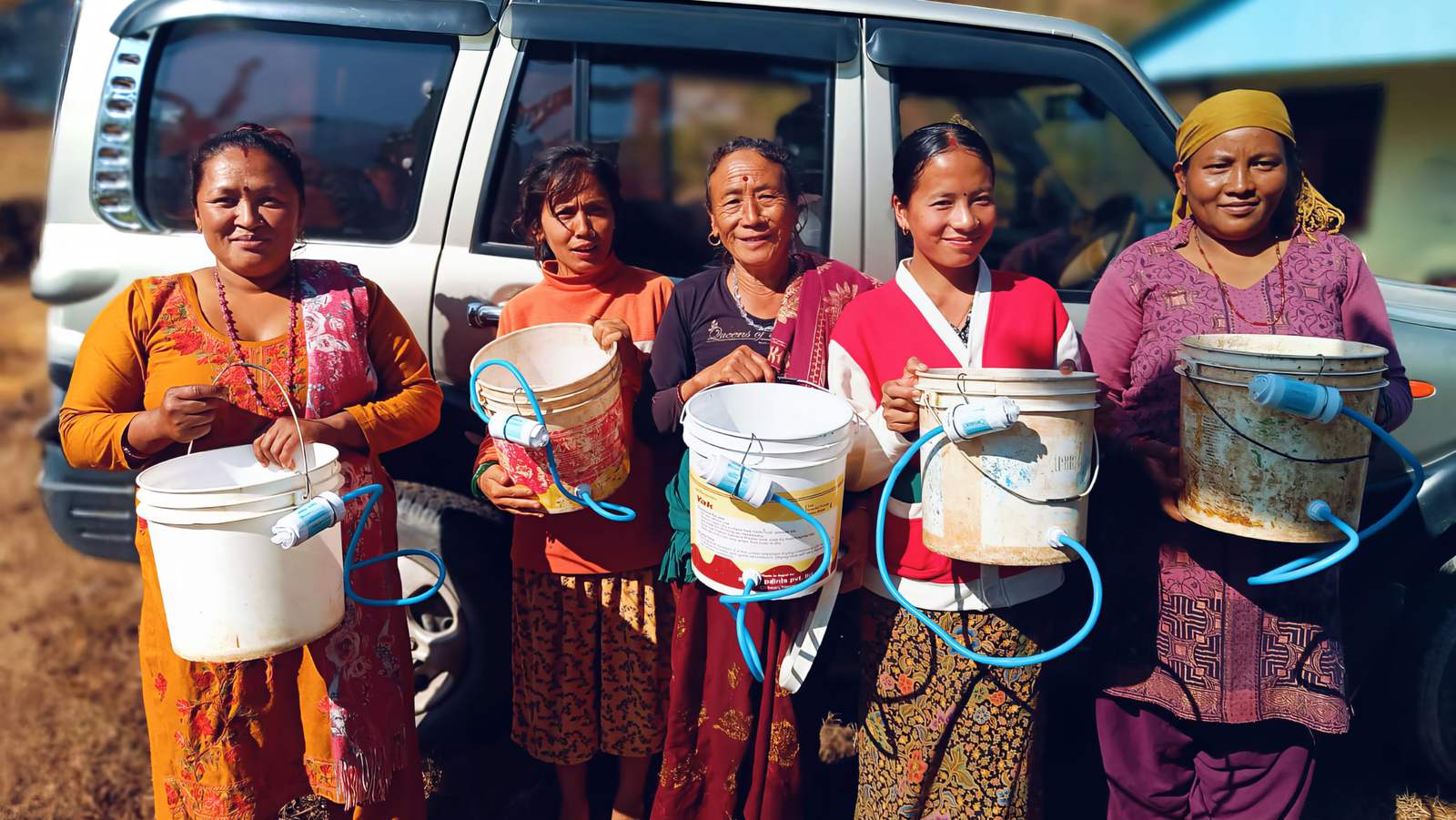 Women in bright saris hold up their new filter buckets