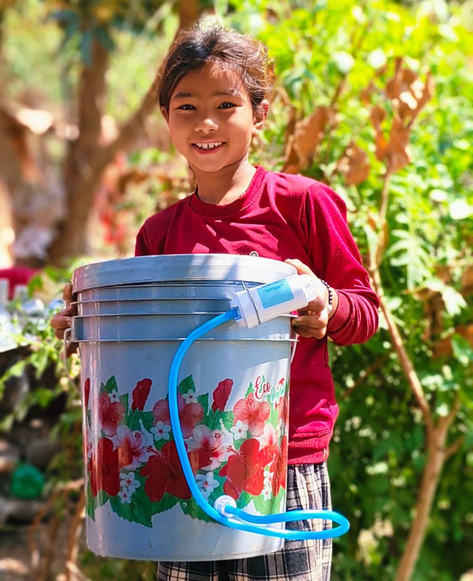A smiling girl holds a filter bucket in her garden